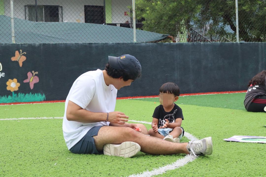 Voluntario acompañando a un niño pequeño sentados en el pasto