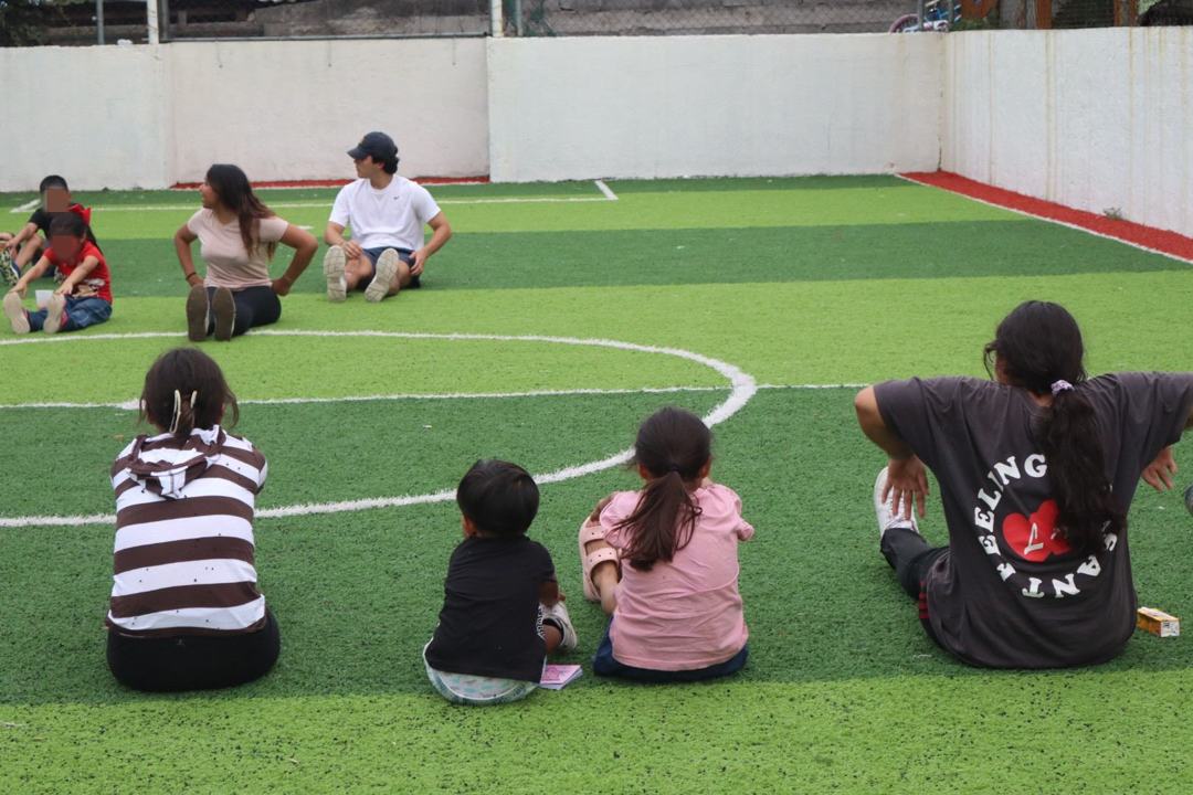 Grupo de niños y voluntarias sentados en la cancha al final de la jornada