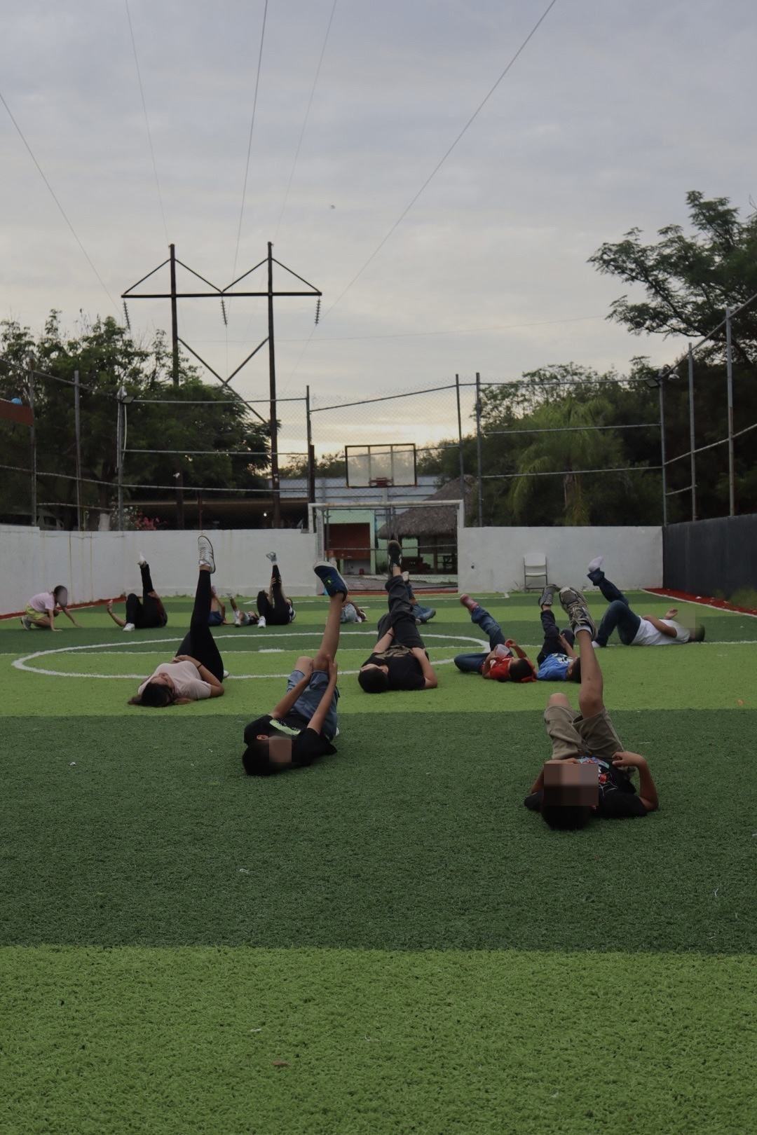 Dinámica grupal de estiramiento en la cancha al atardecer