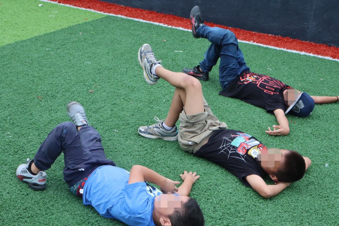 Niños jugando recostados en el pasto sintético