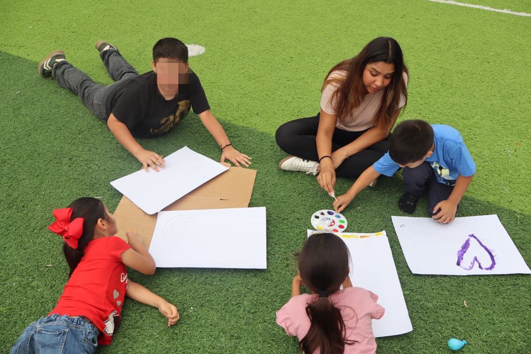 Voluntaria pintando junto a cuatro niños sobre el pasto